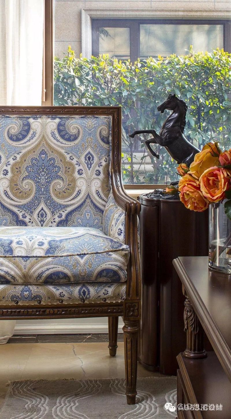 新古典主义风格的菲尔菲克斯沙发椅，拥有精美雕刻的外露实木框和圆形腿，精选的布艺图案为其更添一抹独特的优雅。漆黑的立马摆件立于桦木角桌上，这是一款采用经典几何图案作为整体造型的柱式角桌，极富个性和深度，如梵克雅宝珠宝般的经典四叶草型镶嵌在顶部图案的交汇处，成为点睛之笔。