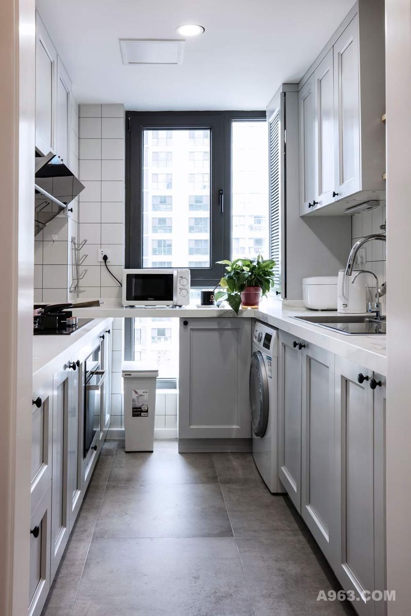 通过大窗户增加整个厨房空间的采光。灰蓝色橱柜搭配大理石台面，墙面全采用瓷砖，方便业主清理油烟污垢。高低台面让业主在烹饪时更省力。