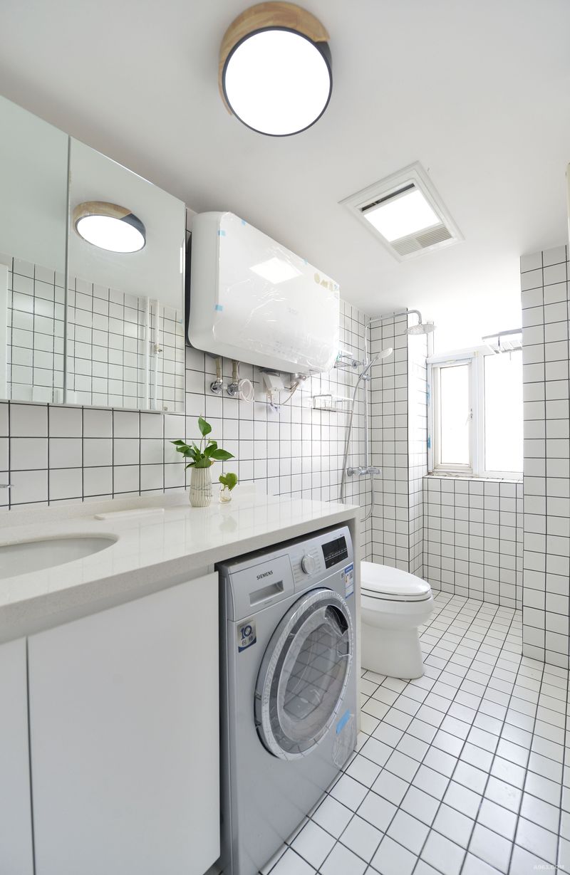 卫生间通体铺装乳白色的瓷砖，特意搭配黑色勾缝。这样在空间上更具有延伸性和立体感，色彩上搭配绿植的点缀也变得无比清新。