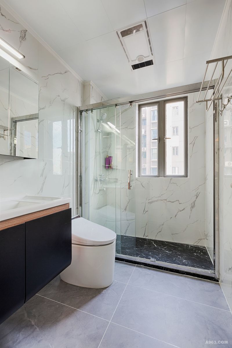 卫生间以白色石纹瓷砖为主体，令卫生间显得更加干净整洁，内部空间纹理和谐而富有韵律。黑色洗手台与卫生间的白色瓷砖形成色差，黑白对比让卫生间色彩层次感加强。淋浴间的透明设计，既达成了干湿分离的功能区划分，三段折叠淋浴间玻璃门，让卫生间显得更加通透开阔，有效缓解了卫生间有限空间带来的压迫感，带来更加舒畅的体验。  
