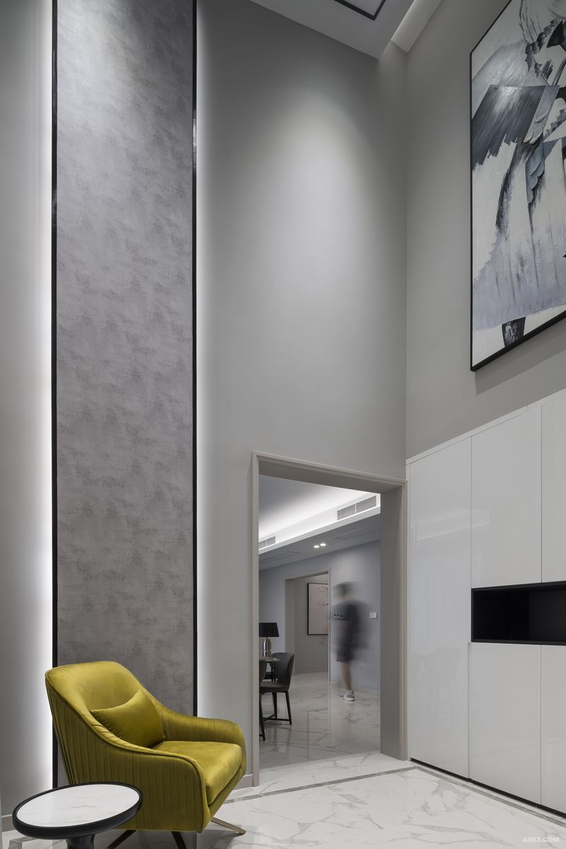 隔断墙体放置正常尺寸顶天立地柜搭配灰白抽象画，弥补灰色挑高空间空白感，放置果绿色沙发椅，可做日常出门更换着装休息等待区，鲜明的颜色作为灰度空间的点睛色彩。