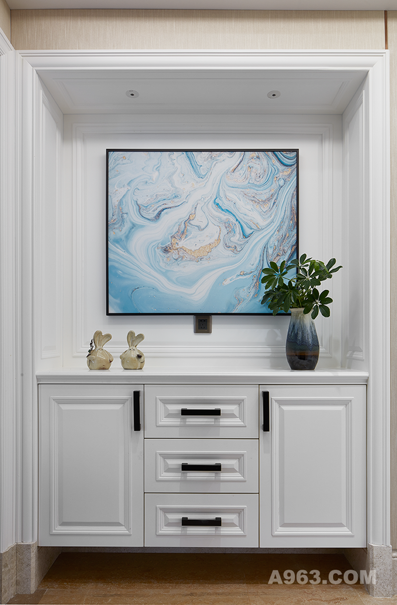 简洁的白色木柜，精致的渐变宝蓝色陶瓷花瓶，金色的兔子摆件体现家装的趣味，随处可见的绿植为这个家庭的居所增加一份生活的写意。方正的格局搭配方正的柜子画框，达到了线条的一致美感。