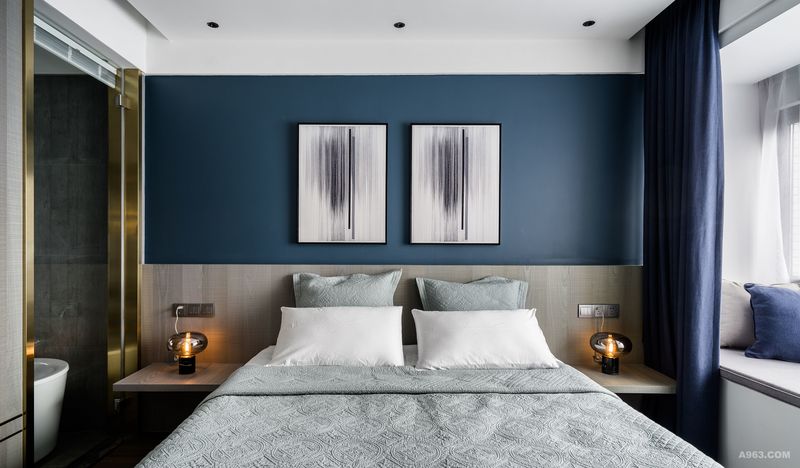 对称式形体修饰，让休息空间在深海蓝的氛围下，更具静谧感。背景墙半乳胶漆半护墙板装饰，悬空板+灯泡造型的床头灯，简洁却不乏设计感。