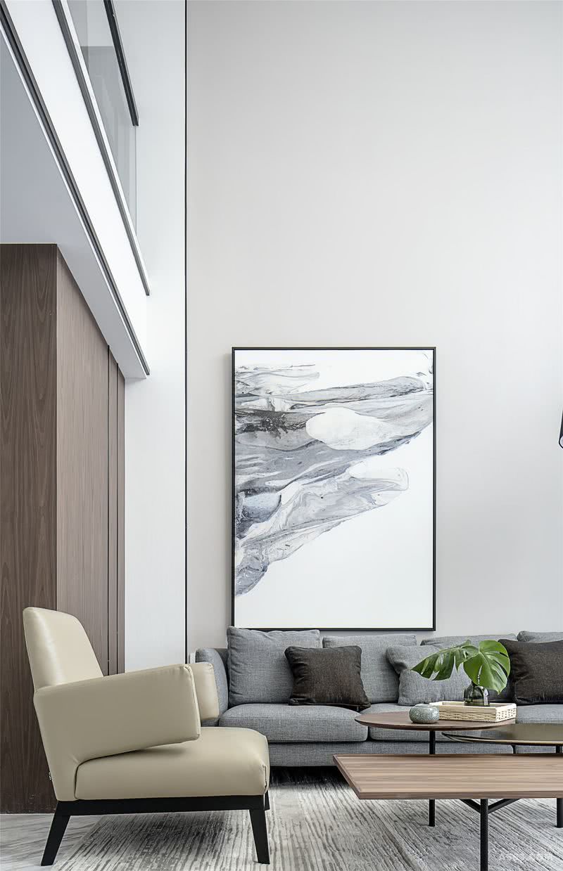 沙发背景墙用的是淡淡的暖灰色刷漆壁布，再搭配大副抽象挂画。挂画意境清逸潇洒，色彩与客厅黑白灰的主色调保持一致，大美无言，妙道自然。

