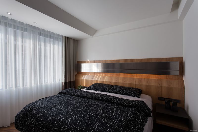 呼應主牆的紋理，主臥床頭主牆則選用實木、鍍鈦合金、間接光源，延續臥眠空間溫潤而時尚的休憩意趣。