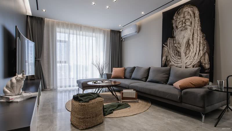 灰色的皮质沙发搭配一抹柔和的暖色调，藤编矮凳与地毯透露着原始的气息，墨绿色毛毯调和整体色调。