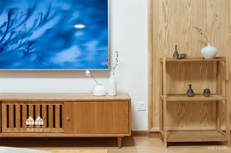电视背景墙本着少即是多的原则大面积的留白，两边以木饰面简单造型搭配，突出禅意的简洁。实木置物架和电视柜以简单素雅的线条配以素色陶瓷瓶和干花。