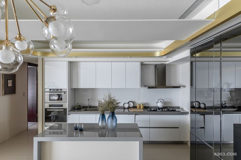 廚房空間以中島作為與餐廳的界定因子，金色的天花線條與白色的媒材勾勒，引述舒適而優雅的區域張力。