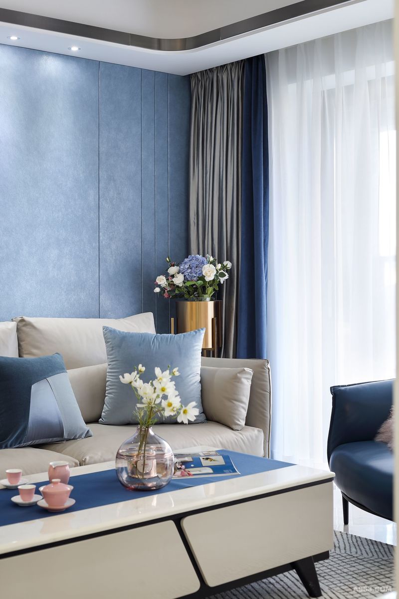 客厅的沙发背景墙采用了雅致的蓝色硬包，与电视背景墙的白色形成强烈的视觉冲击，使空间富有层次。在偏冷的基调上，恰到好处的是水晶球般的落地灯，暖暖的光线，晕开了空间的冷调，将家的温度丝丝沁入其间。