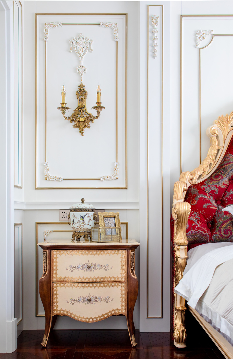 延续客厅的配色，金色和猩红色的丝绒抱枕将床上也装饰得华丽精致。而瓶中的白玫瑰又带来一丝清雅。洛可可式的柔媚浪漫在卧室设计里被表现得淋漓尽致。
