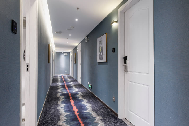 波谱艺术的诙谐与放松体现在挂画与导示上，灰蓝色的墙体还有深蓝色波浪纹理的地毯上的红色线条提亮了整个走廊。