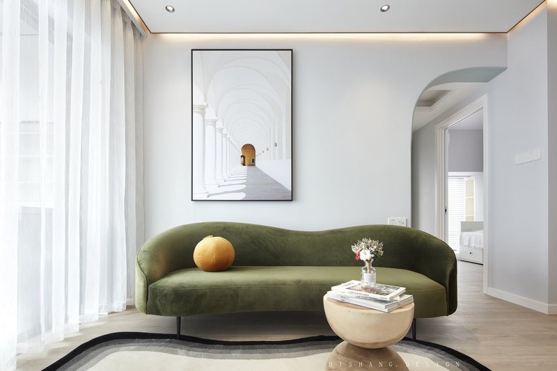 客厅
墙上的挂画，在视觉上延伸空间；莫兰迪绿色丝绒沙发与原木色的漏斗小茶几相搭配，质朴而优雅；阳光通过纱帘洒在沙发上、地摊上，空间愈发治愈。