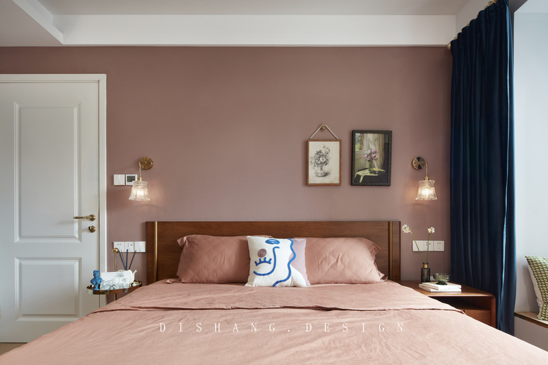 卧室墙面以脏粉色为底色，用白色和金色来描绘居家的形状，再以饱和度高的蓝色调和空间氛围，营造一个温柔、安宁、高级的休憩空间；在软装搭配上更加倾向细腻和温馨，原木双人床、舒适的床上用品、绒面窗帘、对称的复古床头壁灯散发出独特柔软的气质，空间达到平衡。