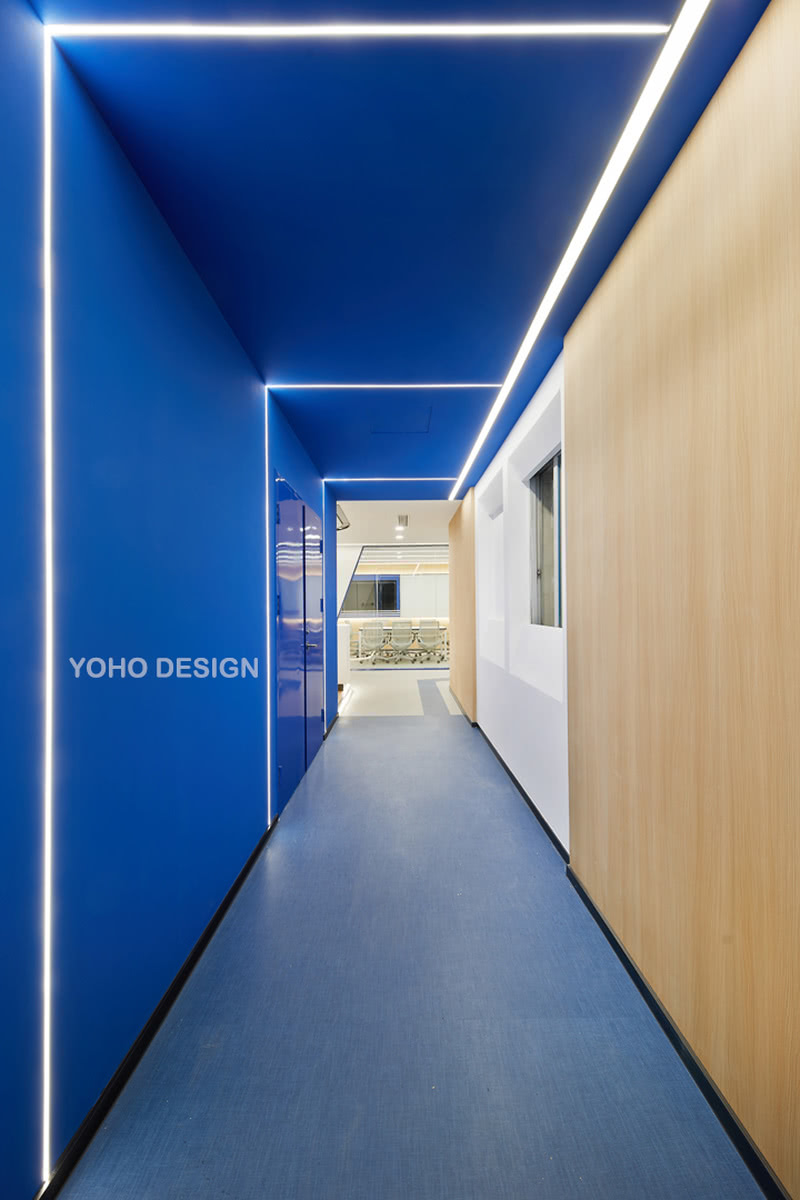 进入办公区域的通道用大片的蓝色为主色调，突出醒目的色彩将人们的注意力都吸引到了这面墙上；线性灯作为设计亮点修饰墙面，无不透露着与科技、未来空间息息相关的格调。