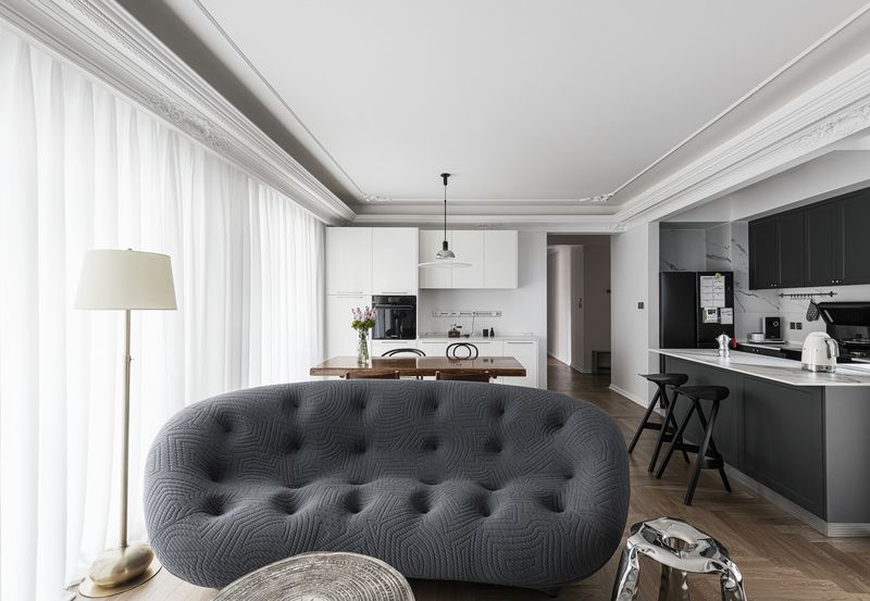 干净柔和的白色与知性时尚的灰色构成了客厅的基础色调，暖色系的木质地板调和其中，营造出温馨的居住氛围。整个室内空间的天花板都能看到角花的运用，在无意间描绘着法式浪漫。
Ligne Roset沙发搭配Eichholtz银色茶几，现代家居与法式复古的结合相得益彰，圆润饱满的曲线拥有充实的质感，兼具美观与实用。