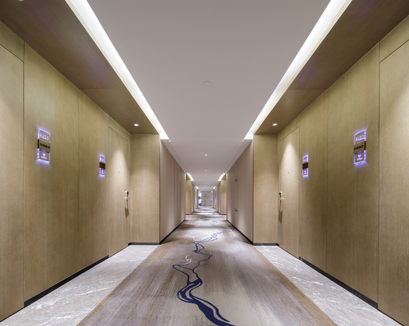 通往各房间的走道里，没有做过多的装饰和陈设。大面积的原木色，旨在令住客“回归自然”，地毯上深蓝色弧线蜿蜒前进，似乎像流水般在引导着宾客的前进。
