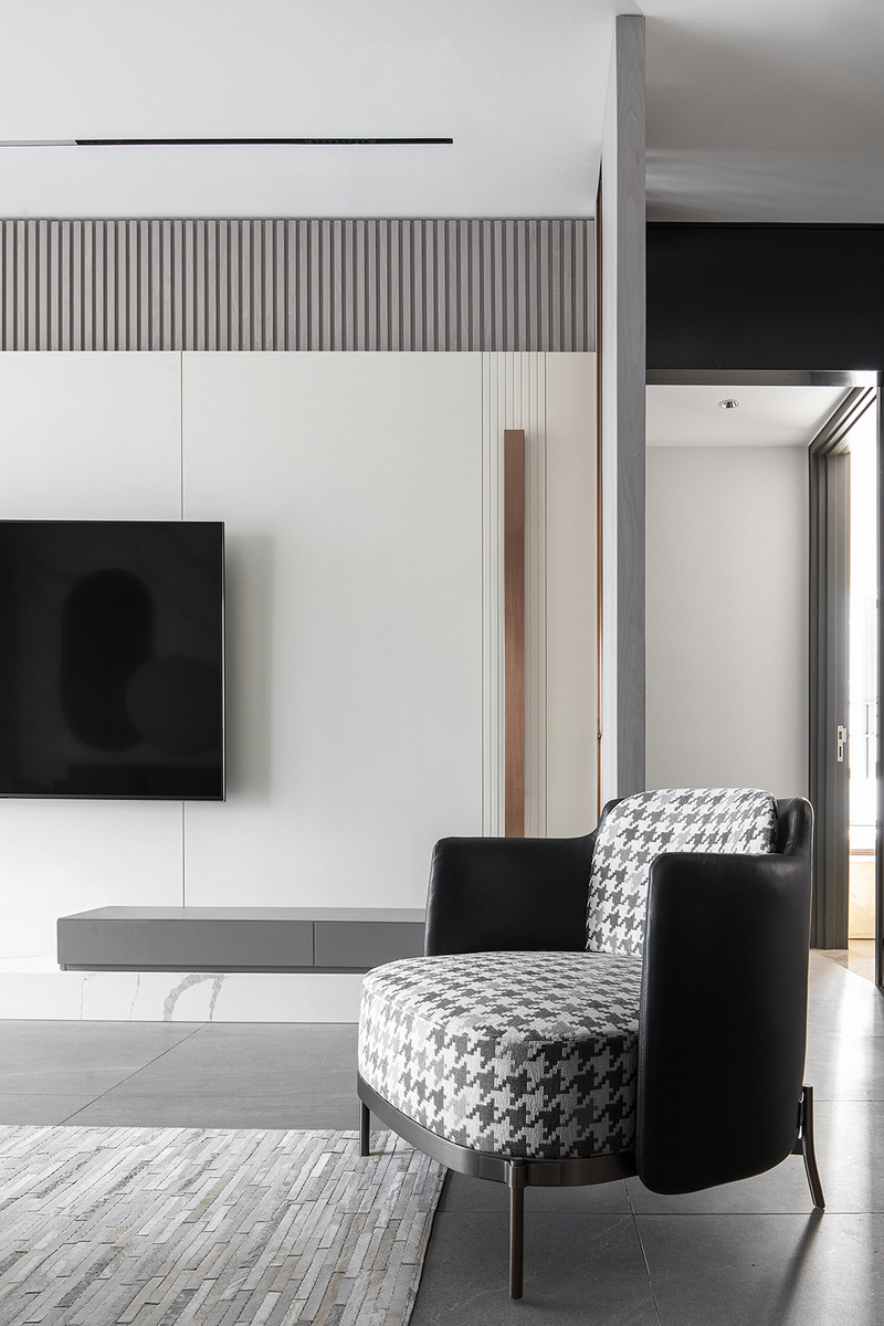 时尚个性的黑白灰基底，穿插使用优雅的灰咖色，构成了客厅空间的色彩基础。电视背景墙富有层次，由大理石+木搁栅+混油护墙板构成，自下而上根据黄金比例进行造型设计。
