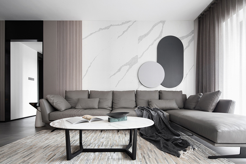 沙发背景墙由清晰纹理的浅色岩板+灰咖色木格栅及硬包构成，其上不再以挂画作为装饰，而是由一对圆形铁艺相互叠加凸显局部亮点。
