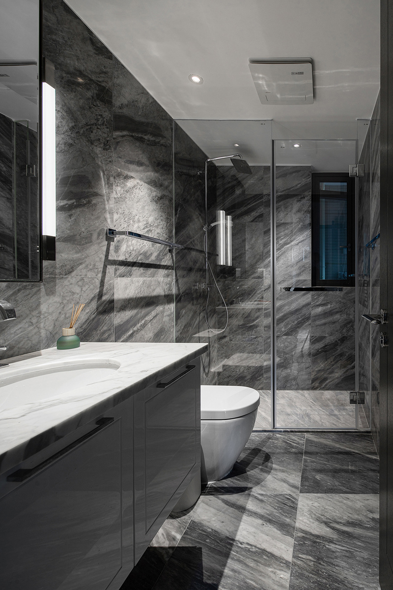公卫墙地面通铺深色纹理的大理石，洁具选用白色简约经典款，淋浴房则采用极简的无边框款式，放眼望去，仅由黑白构成的卫浴间显得十分干净、通透。
