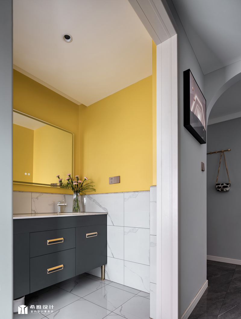 公卫干湿分离，干区的浴室柜有1.5米长，满足全家人的 需求。因为这个区域采光弱，空间湿冷，为了营造温暖的氛围，墙面采用的半高鱼肚白瓷砖搭配黄色墙漆，把这个区域提亮起来，让人觉得明亮又温暖。