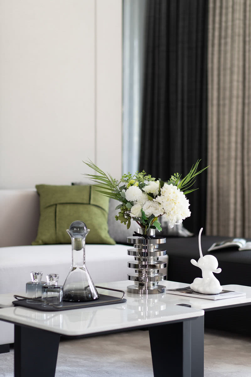 
黑色金属与浅色大理石构成的茶几呼应着黑白相间的沙发，调动着整体起居空间的风味。在设计师的当代手法下，极富肌理色彩的绿色布艺装置与米灰色的墙面，勾勒出高级的线条感和自然质朴的氛围。
