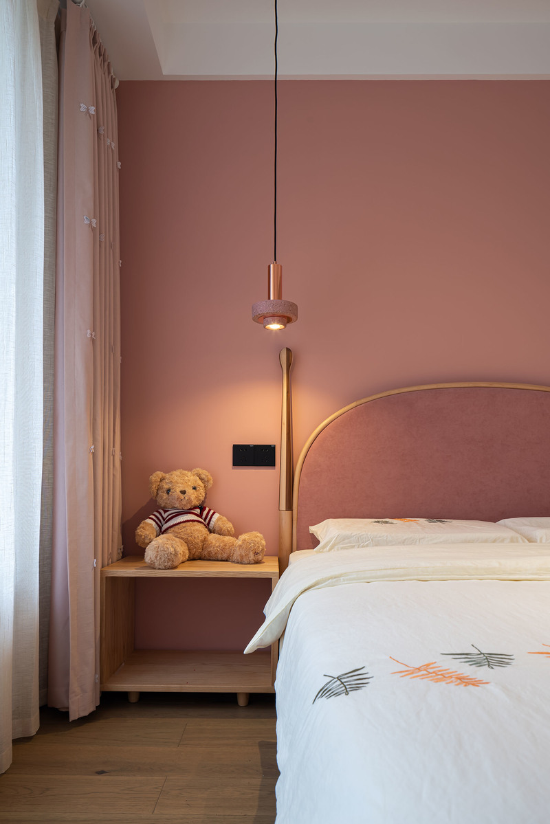 粉嫩的背景墙与深粉的床头形成巧妙的色彩层次，把“粉”的温柔诠释到极致，甜而不腻，温馨十足。垂旋式床头灯以光影氤氲浪漫，形成简约高雅的空间秩序。
