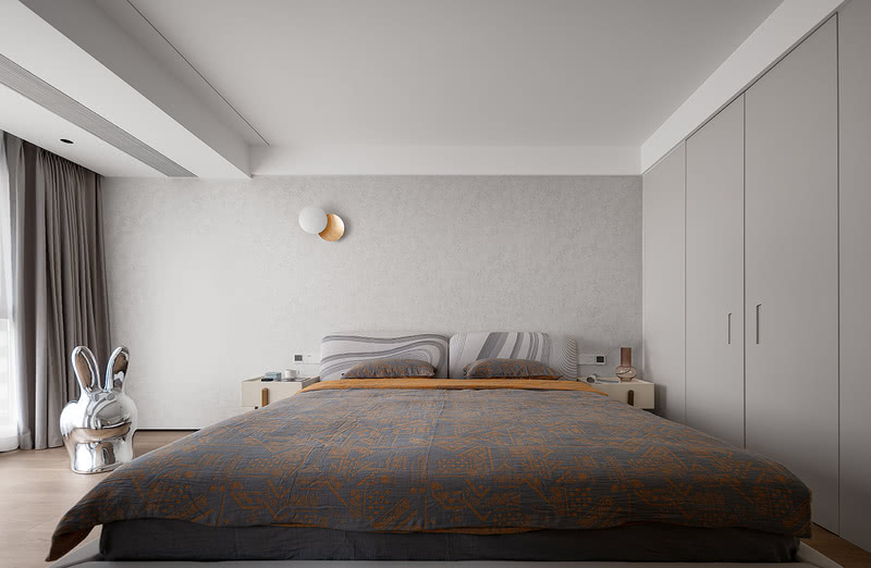 独立于二层的主卧室延续了整体简约纯粹的艺术氛围，也为主人的睡眠环境凭添很多轻盈、丰富的视觉层次。主卧以整柜的形式做了两面墙体，有着绝佳的收纳能力，让整体空间在美观的同时也兼具超强的功能性。床品和寝具则选择了优雅的橘金色和淡蓝色作为搭配，品质整体提升。

