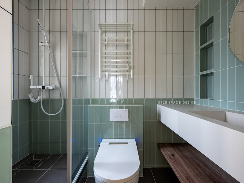 卫生间用绿色瓷砖做半墙拼接，地板用灰色瓷砖起到下沉的视觉效果。淋浴区的高度不变，用玻璃门隔断区域。