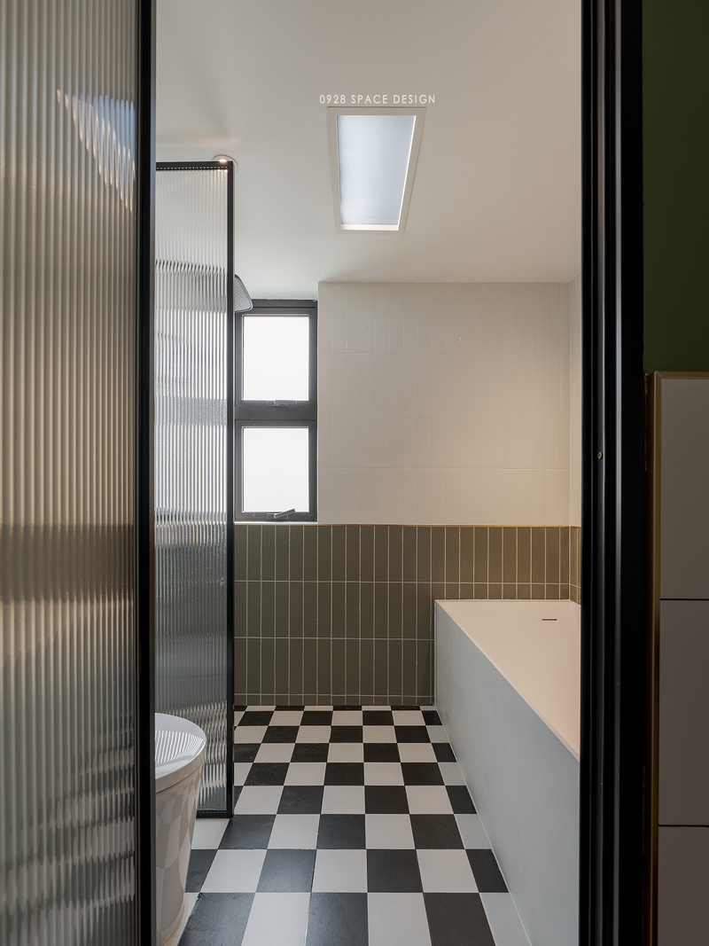 浴室以橄榄绿与白砖上墙拼色，地板与厨房地板砖一致，黑白棋盘格提升整体灵动性。内设有浴缸和淋浴两种洗浴模式，淋浴区与马桶用玻璃隔断。