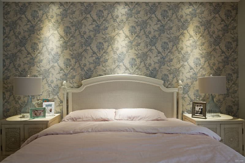 主卧室的珍珠白色镂空实木床有一丝田园的亲切感，米灰色玻璃台灯清爽简洁，床架柱子的雕花质感延展到做旧的床头柜上。