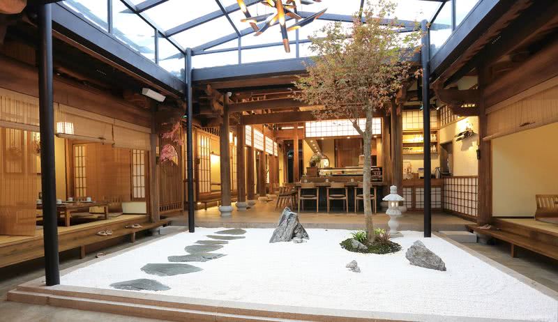       入门前厅利用原有的天井区设计成日式的枯山水造景，形成区域视觉中心。天井引入自然光，使用餐空间变得更加通透，同时也起到节能的作用。