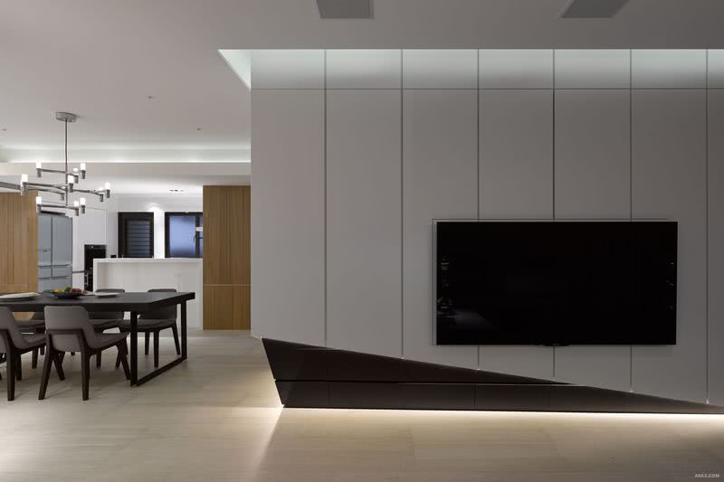 客廳主牆利用木作、燈光，以幾何造型環繞著開放廳區，其上下處以線性的間照效果，有效的營造量體本身的輕盈感受。