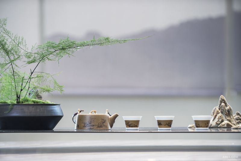 茶艺区
售楼处特设有一个僻静之所作为茶艺区，榫卯结构的的木材与散发着粗粝之美的大理石结合，独特的茶桌是日式与中式的共同演绎。自然简洁、朴素安然，背景墙饰以灰色的垂帘，山水气韵层层漾开，景色似含烟雾，空蒙氤氲，和着名茶的清香，将思绪和心情铺开。茶台底部发出淡淡光晕，古雅的书架伫立一侧，增添了空间简约沉静的气质。